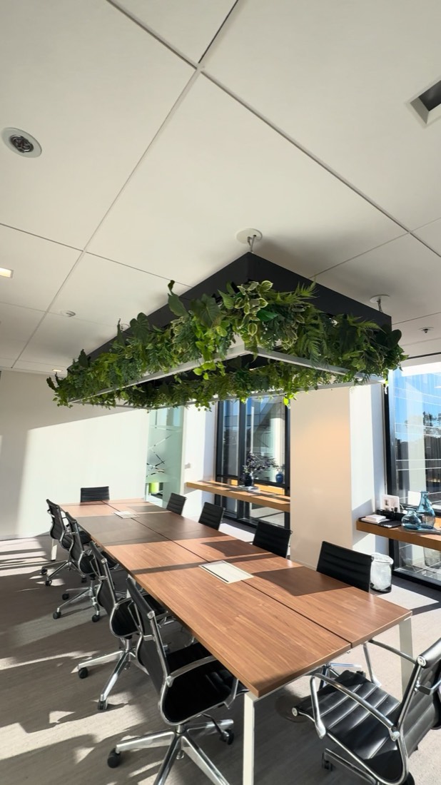 Suspended planter frame overflowing with greenery above a bright boardroom table